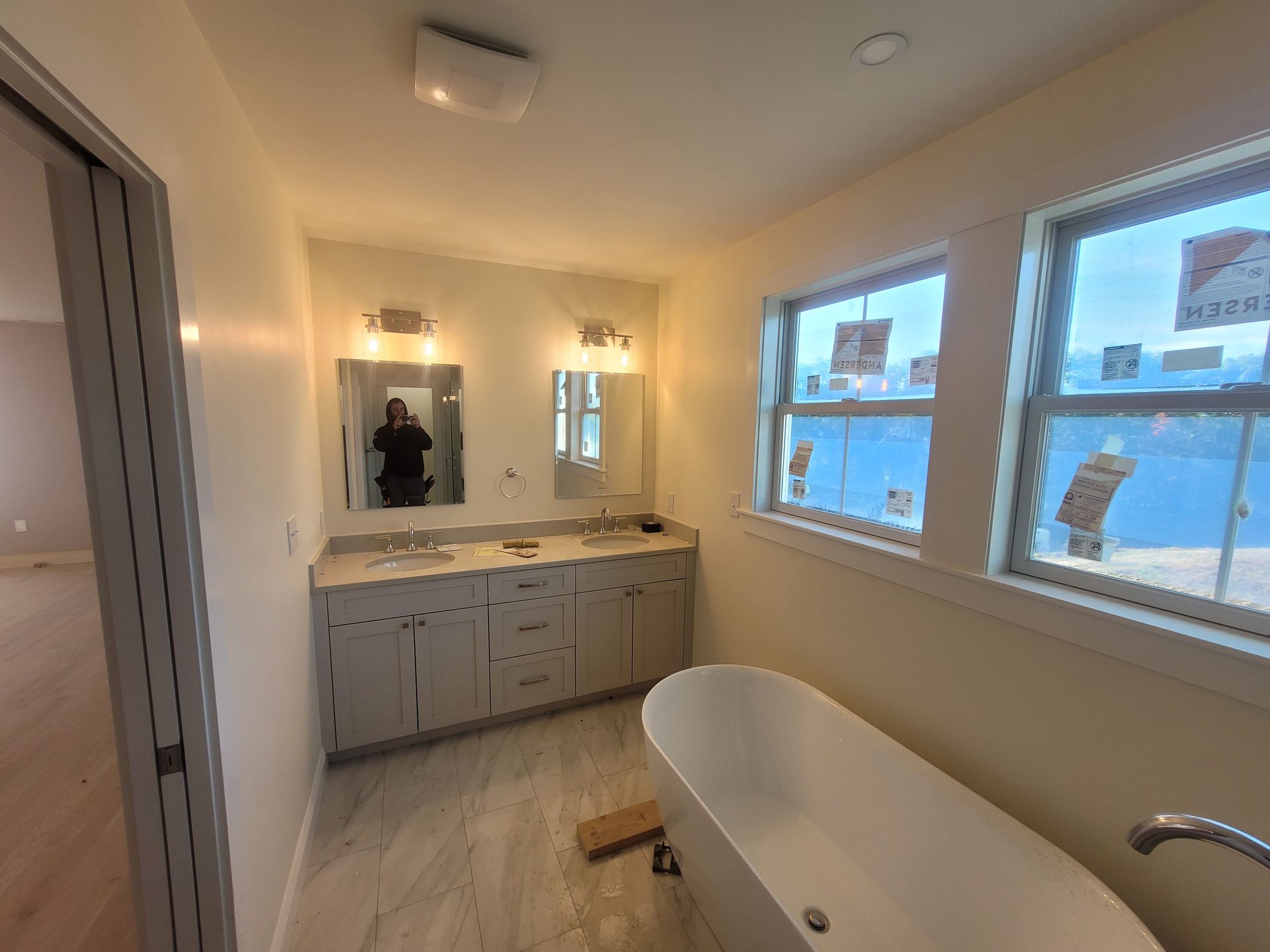 A bathroom with a tub, sink, mirror, and windows.