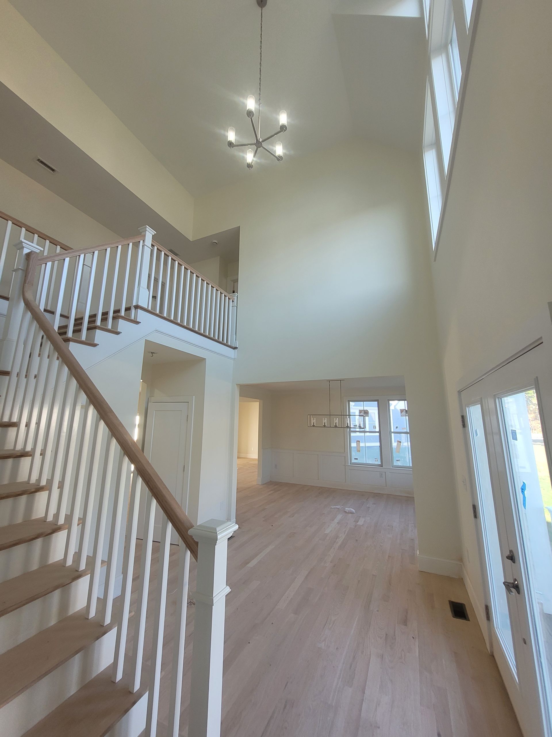An empty house with stairs and a chandelier hanging from the ceiling.