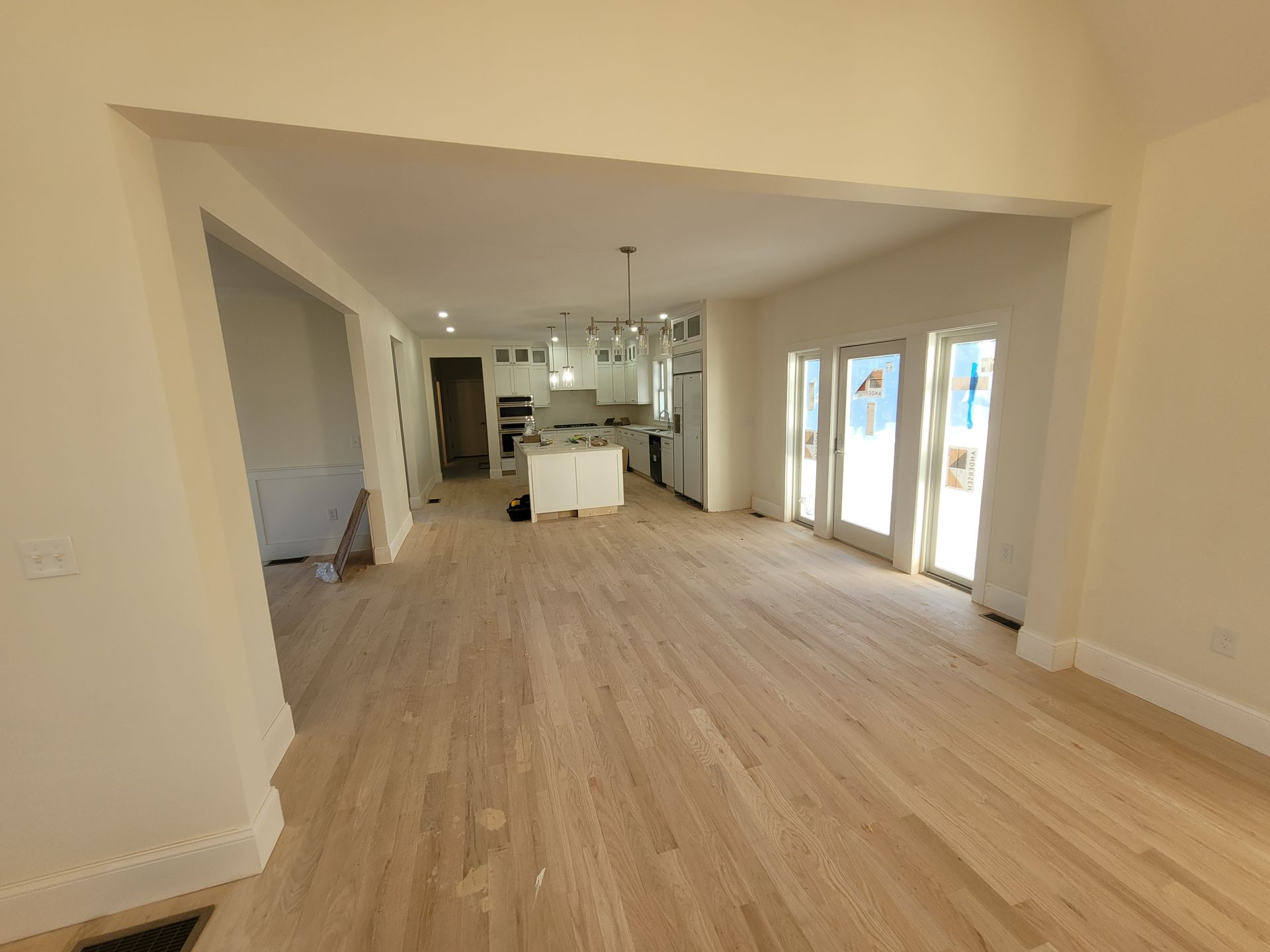 A large empty room with hardwood floors and a kitchen in the background.