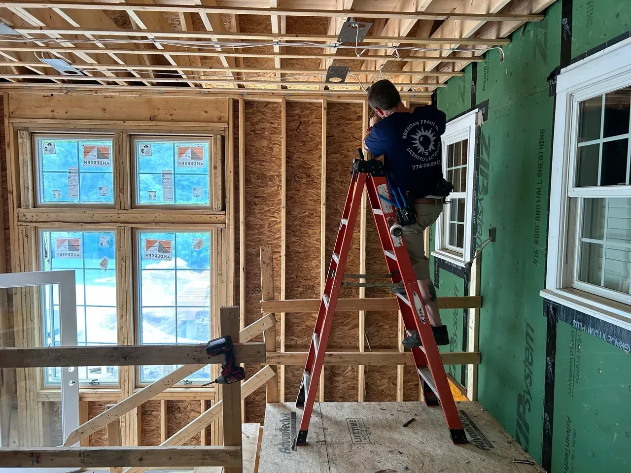 A man is standing on a ladder in a room under construction.