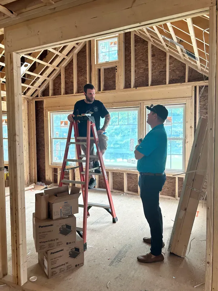 Two men are standing in a room in a house under construction.