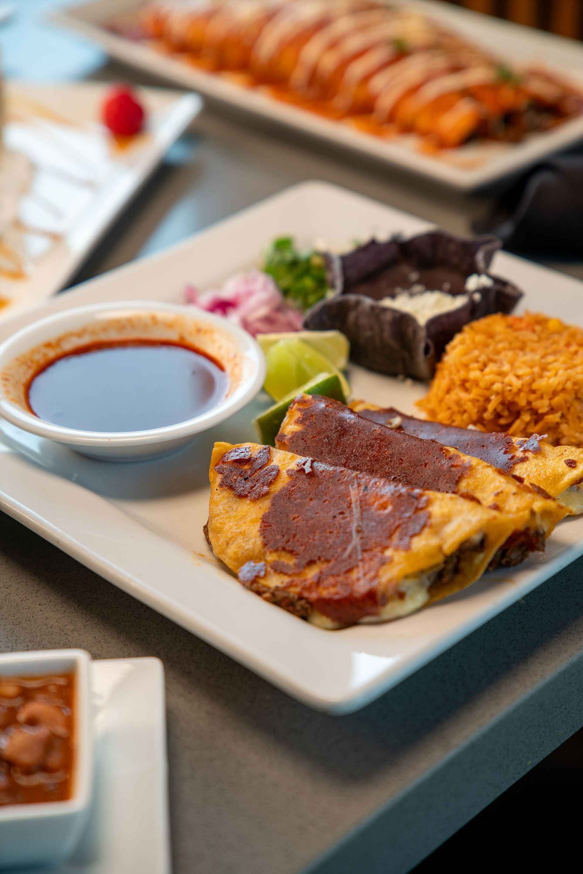 Plate of Mexican food: quesadillas, rice, beans, dipping sauce, lime, and red onions.