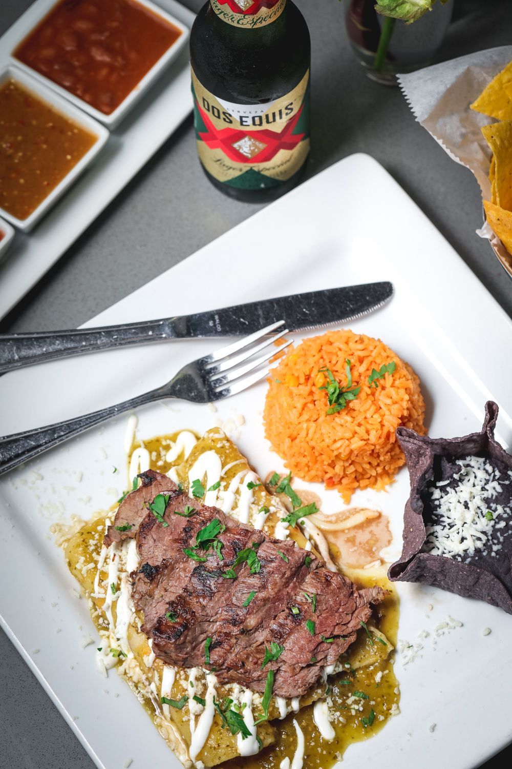 Plate with steak, enchiladas, rice, tortillas, and salsas; beer bottle.