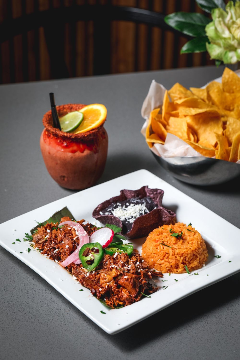 Mexican meal with shredded meat, rice, beans, chips, and a drink.