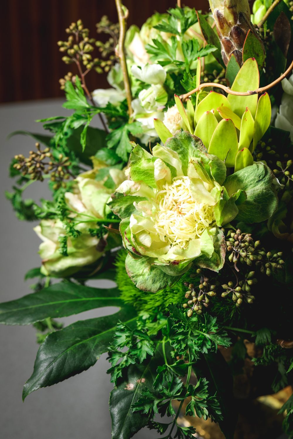 Close-up of a flower arrangement with white and green flowers, various greenery, and brown branches.