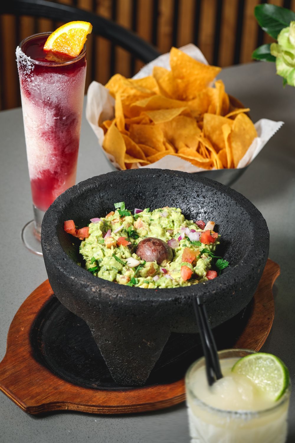 Guacamole in a black bowl with chips, drinks on a table.