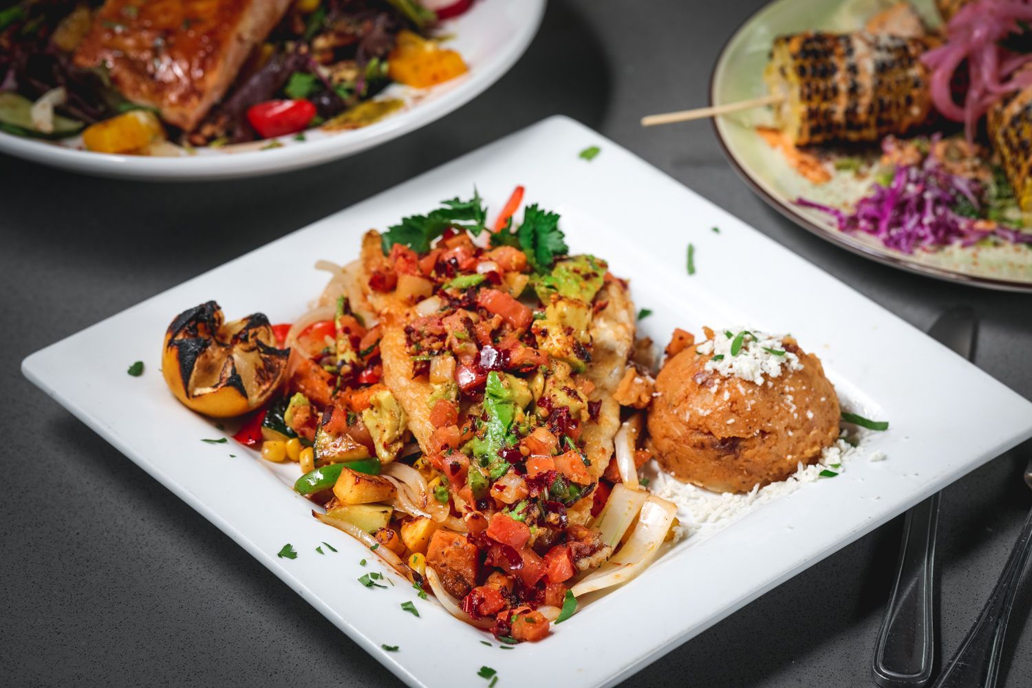 Grilled fish dish with salsa, avocado, and refried beans on a white plate.
