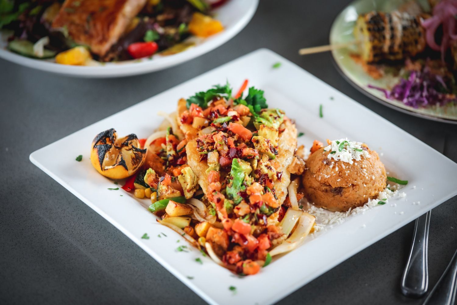 Plate of food with grilled fish, salsa, and refried beans, with a side of corn.