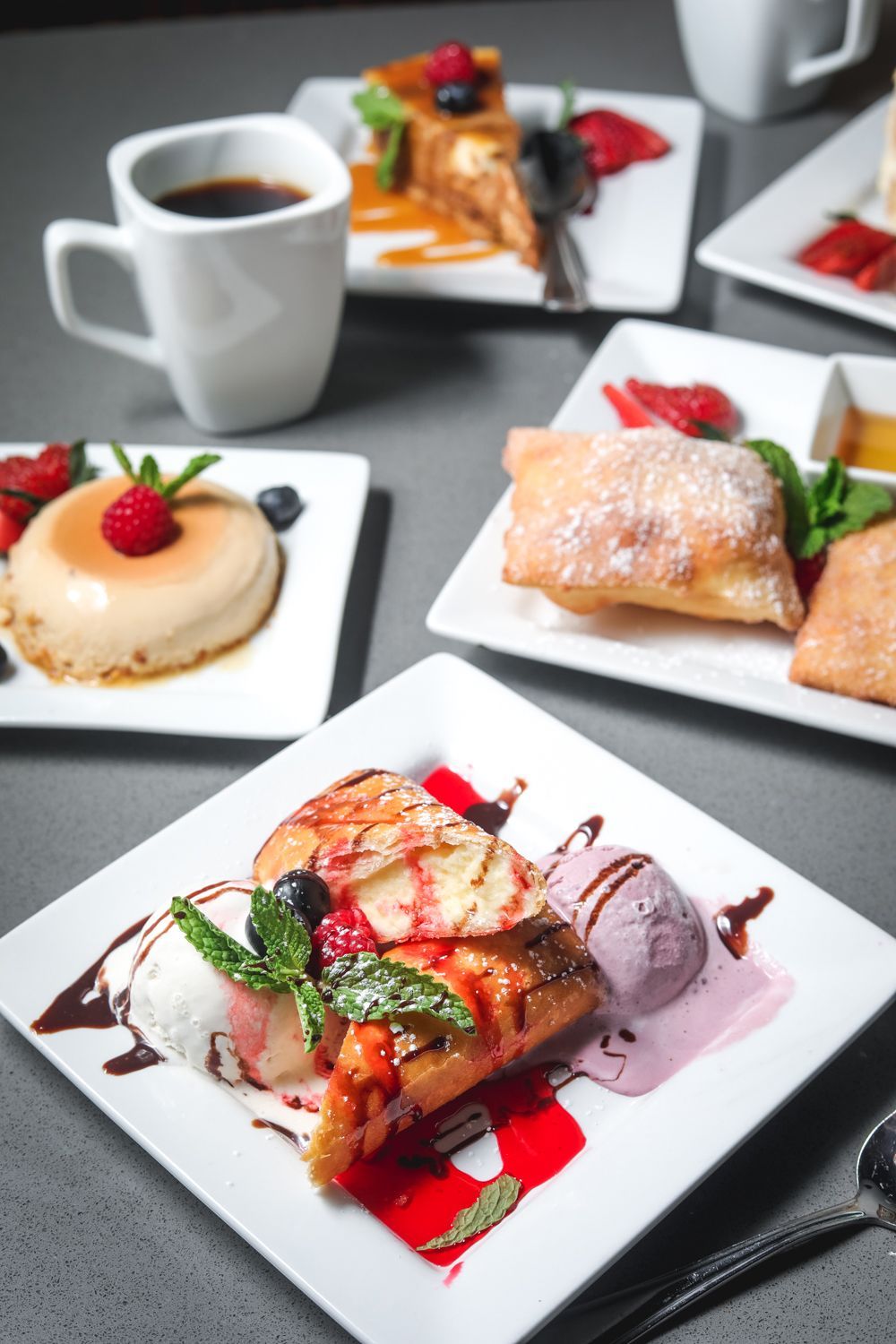 Assortment of desserts on white plates: flan, French toast, fried pastry, with coffee and various toppings.