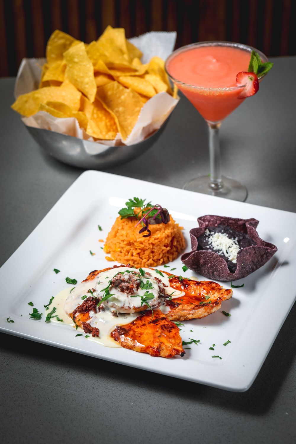 Plate of Mexican food: chicken with sauce, rice, beans, chips, and a cocktail.
