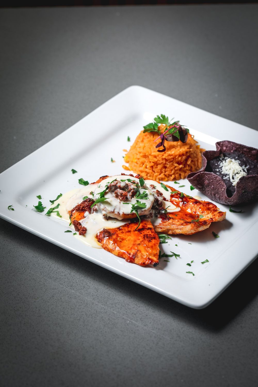 Grilled salmon with white sauce, rice, and purple corn chips on a white plate.