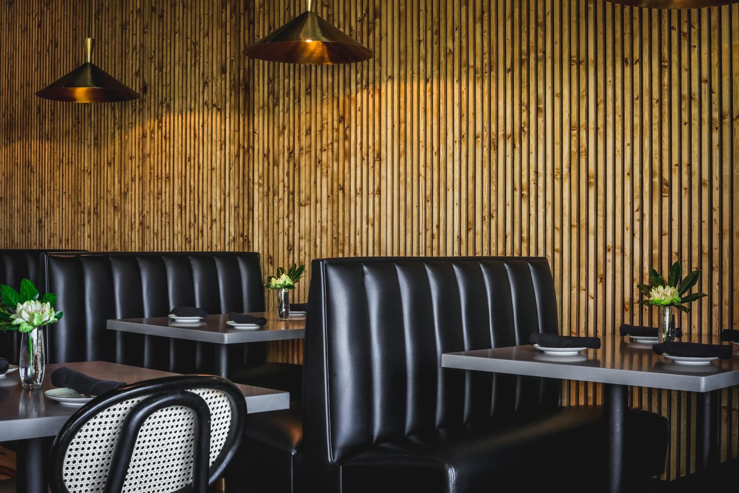 Restaurant interior with black booths, wood paneling, tables, and pendant lights.
