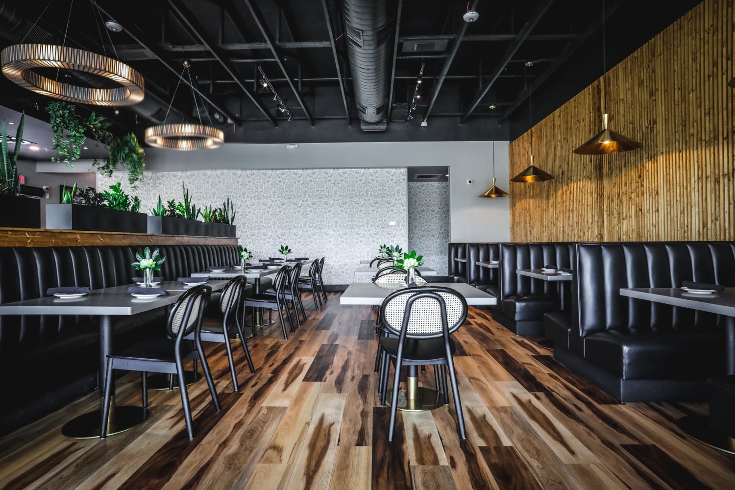 Restaurant interior with wooden floor, black booths, tables, and textured walls.