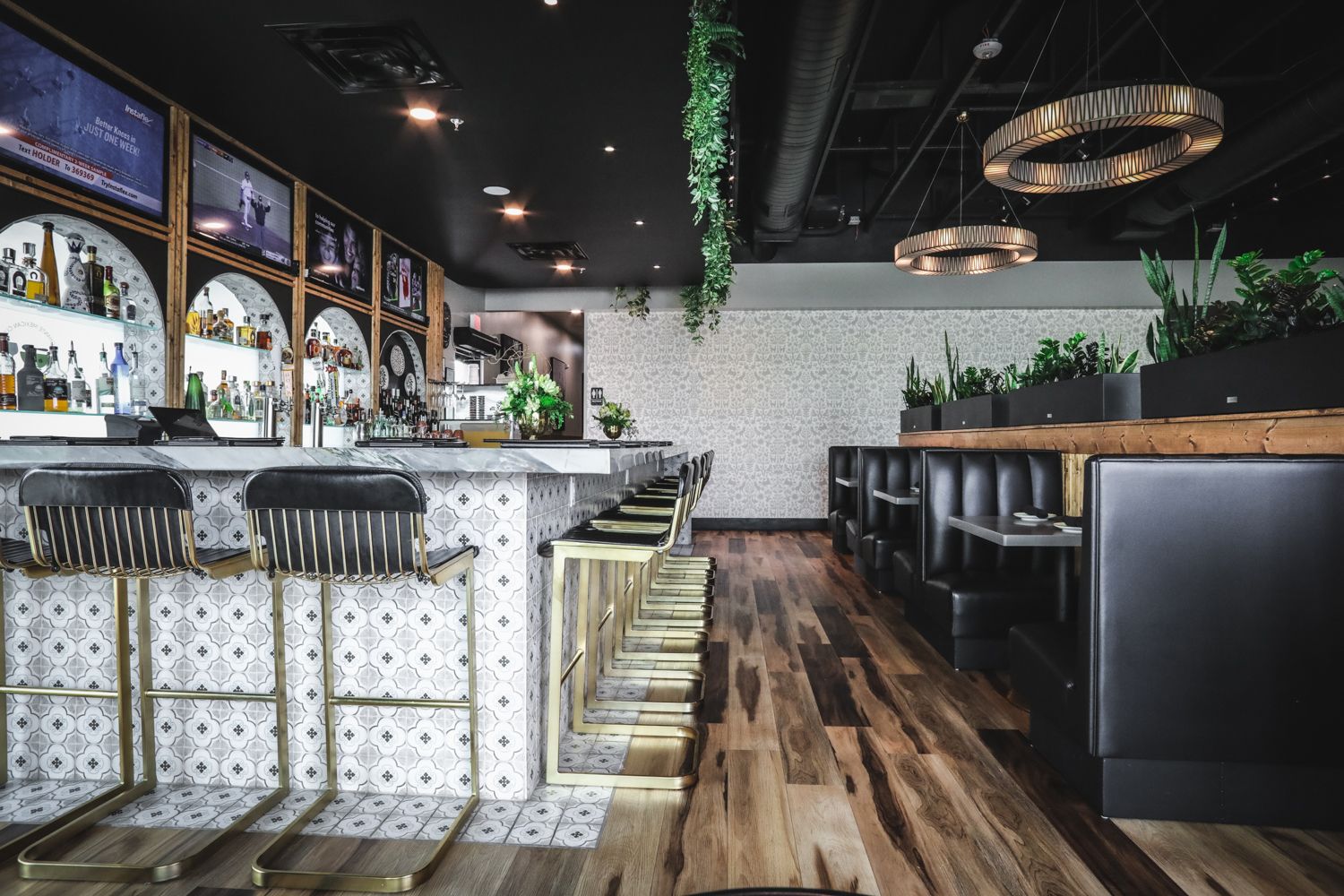 Bar interior with marble counter, gold stools, booths, and plants.
