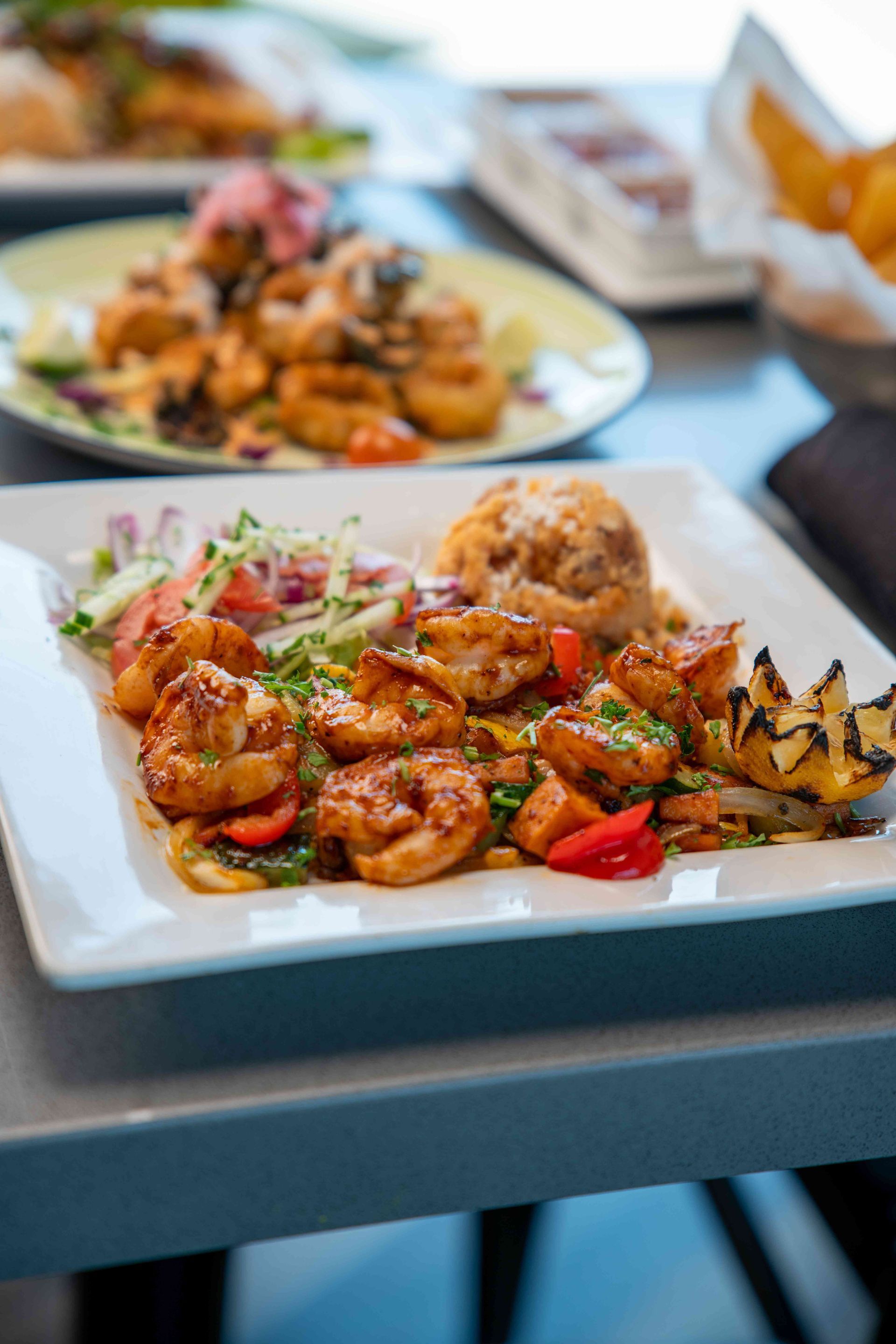 Plate of seasoned shrimp with vegetables and rice, other dishes in the background.