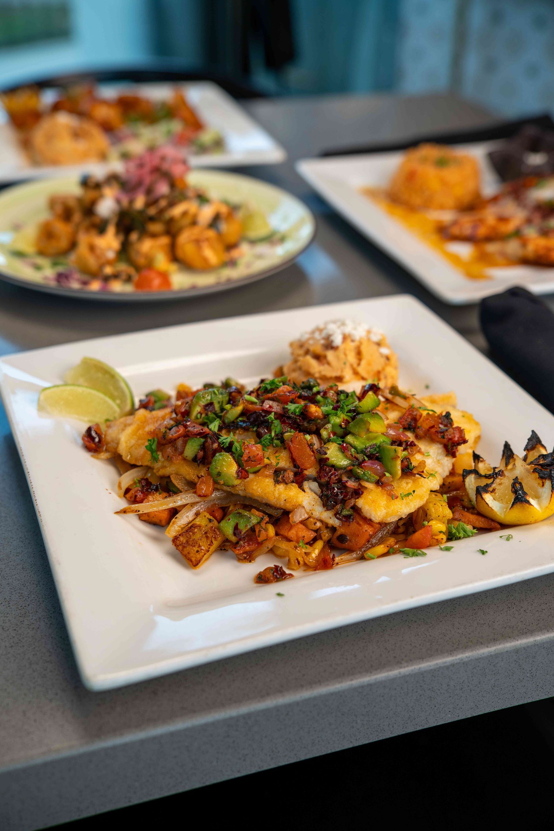 Plate of food with fish and topping, other dishes in background.