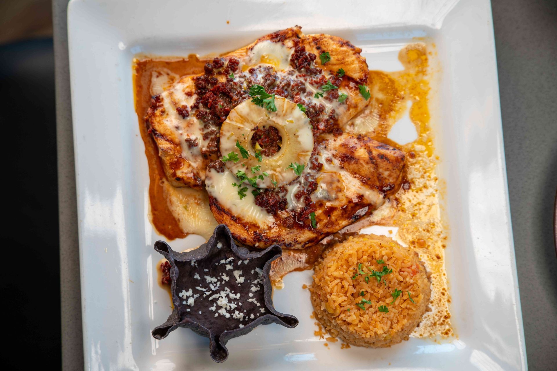 Chicken dish with pineapple, chorizo, rice, and sauce on a white plate.