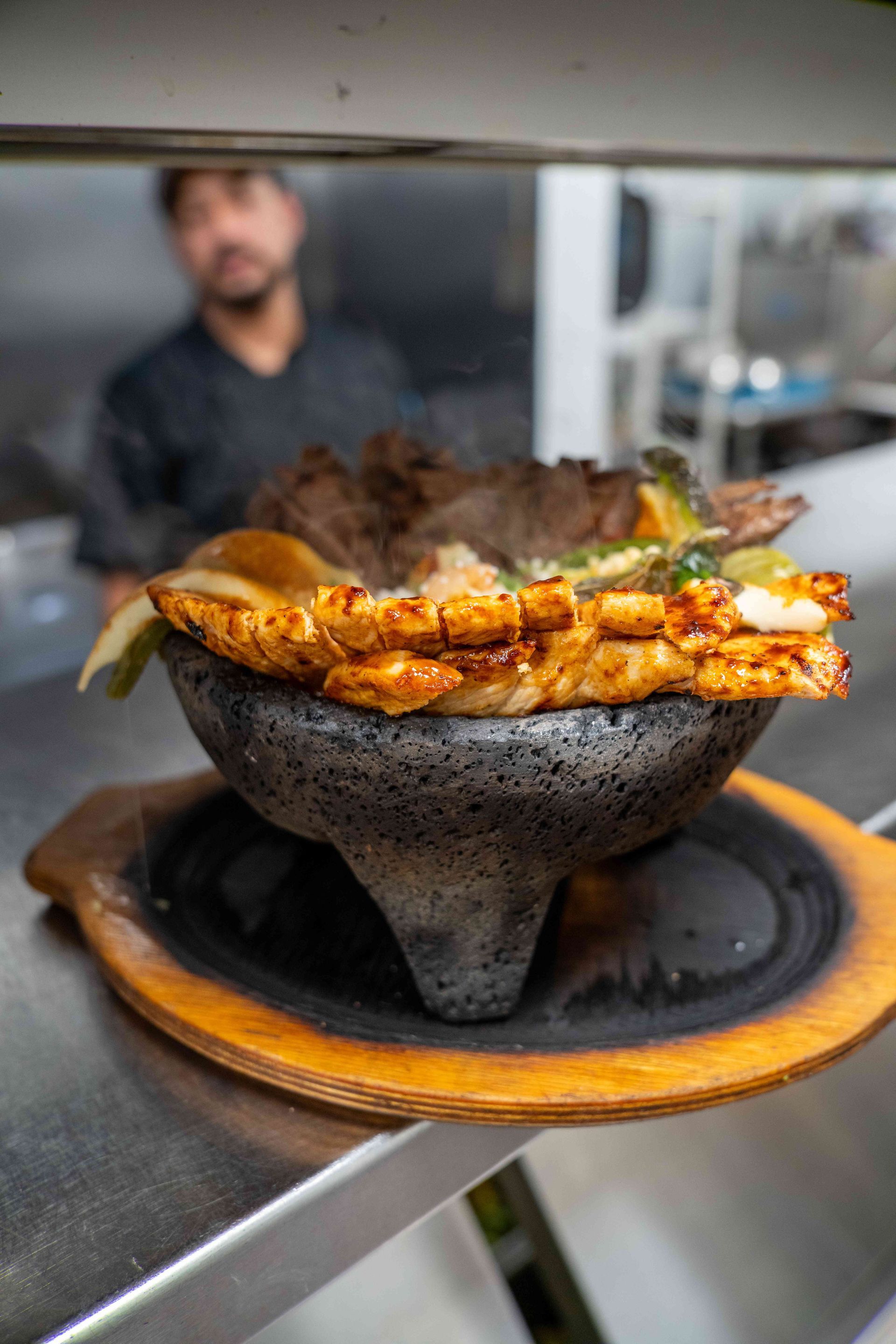 A sizzling molcajete bowl filled with grilled meats and vegetables, held by a person in a restaurant.