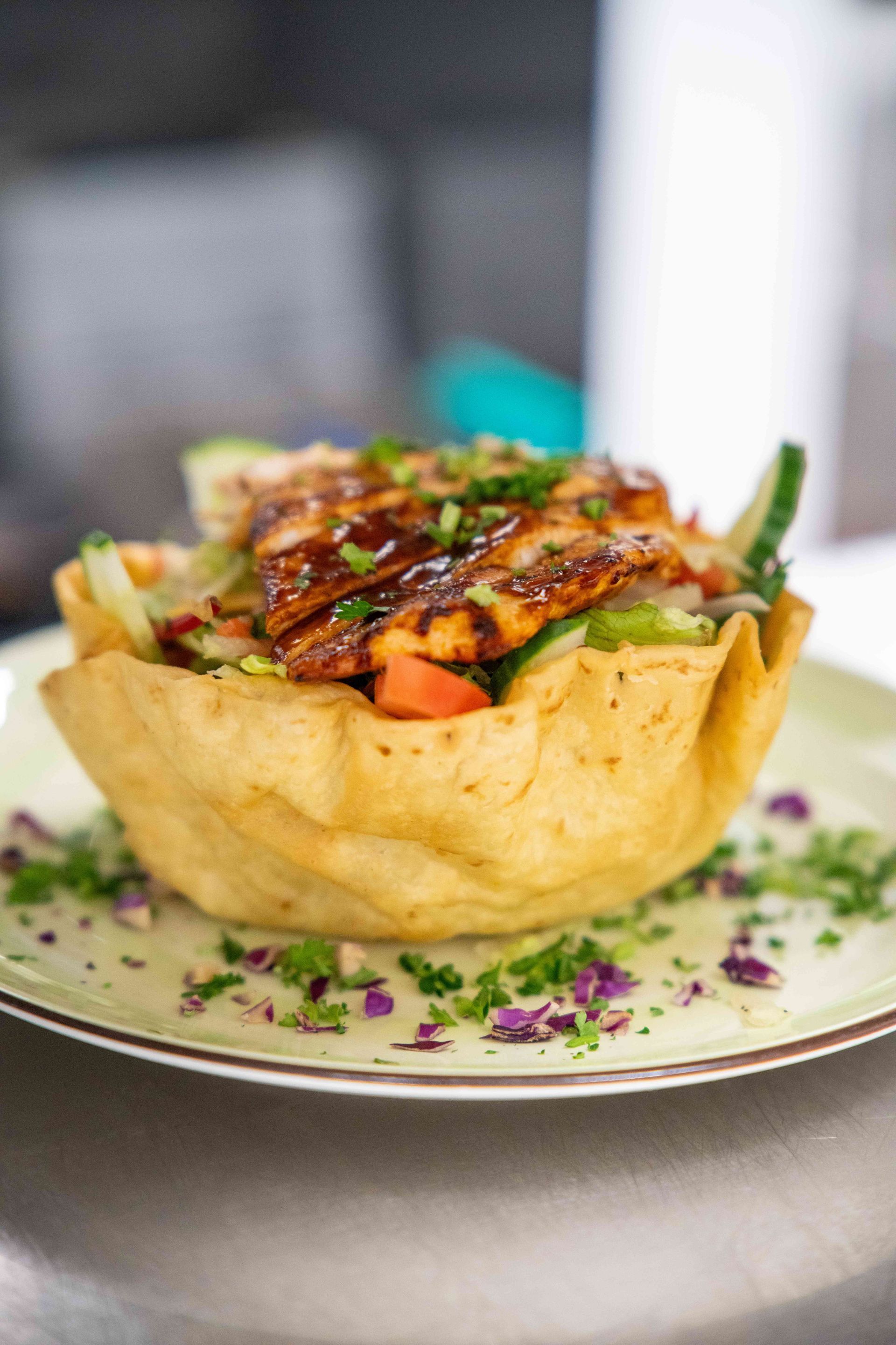 Chicken salad in a tortilla bowl, drizzled with sauce, on a plate, garnished with herbs.