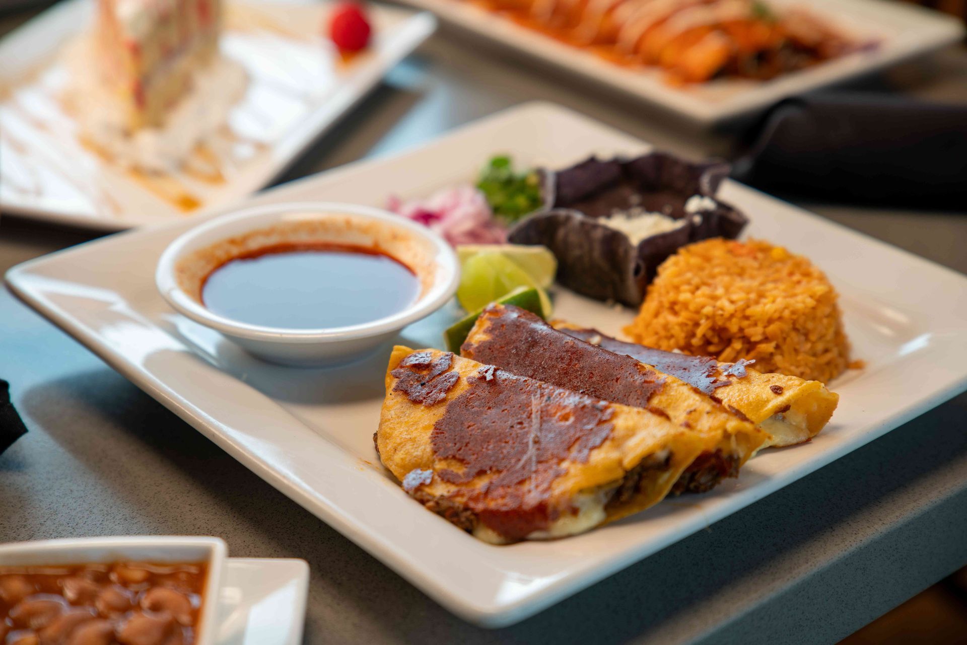 Plate of Mexican food: tacos, dipping sauce, rice, beans, lime, and garnish.