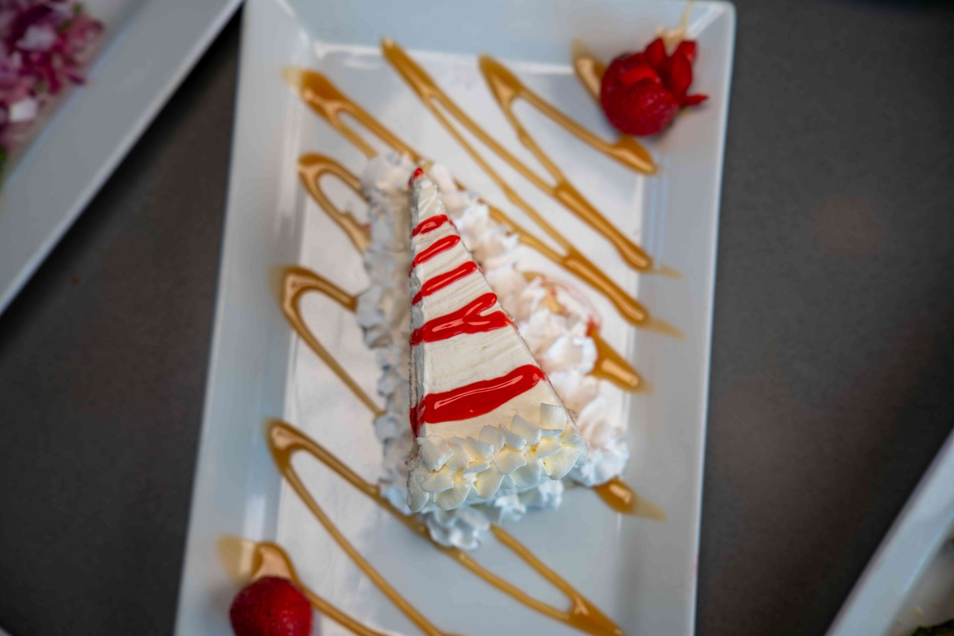 Slice of cake on a white plate, drizzled with caramel and topped with whipped cream and strawberries.