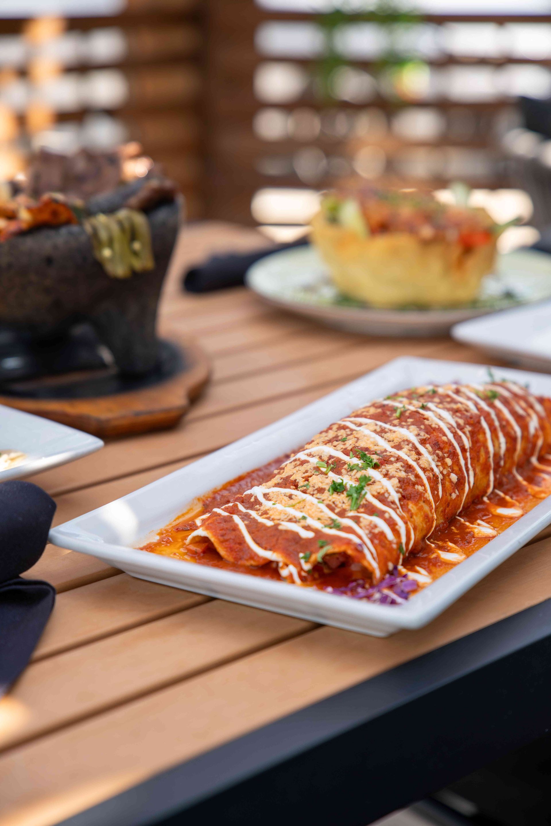 Burrito covered in sauce on a white plate, served outdoors on a wooden table.
