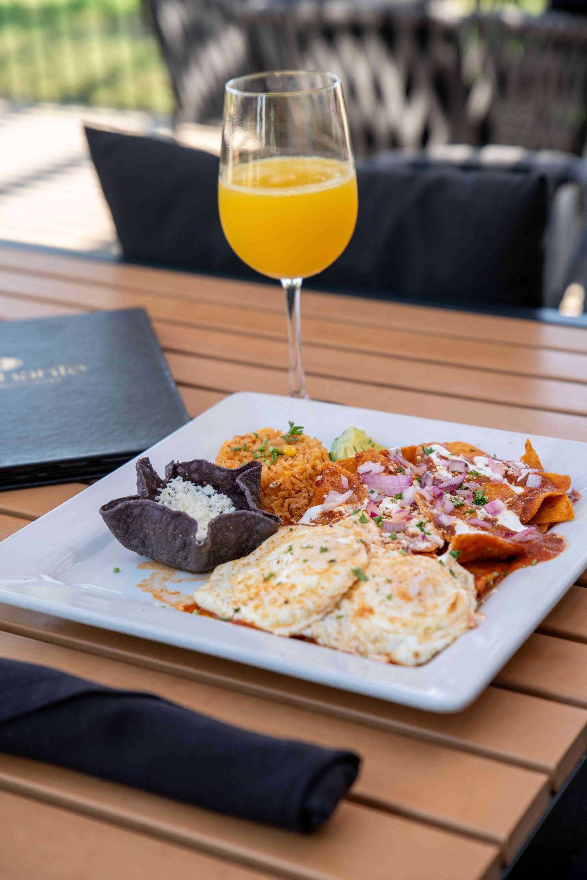 Plate of food with sunny-side-up eggs, chilaquiles, black bean, and drink on a wooden table.