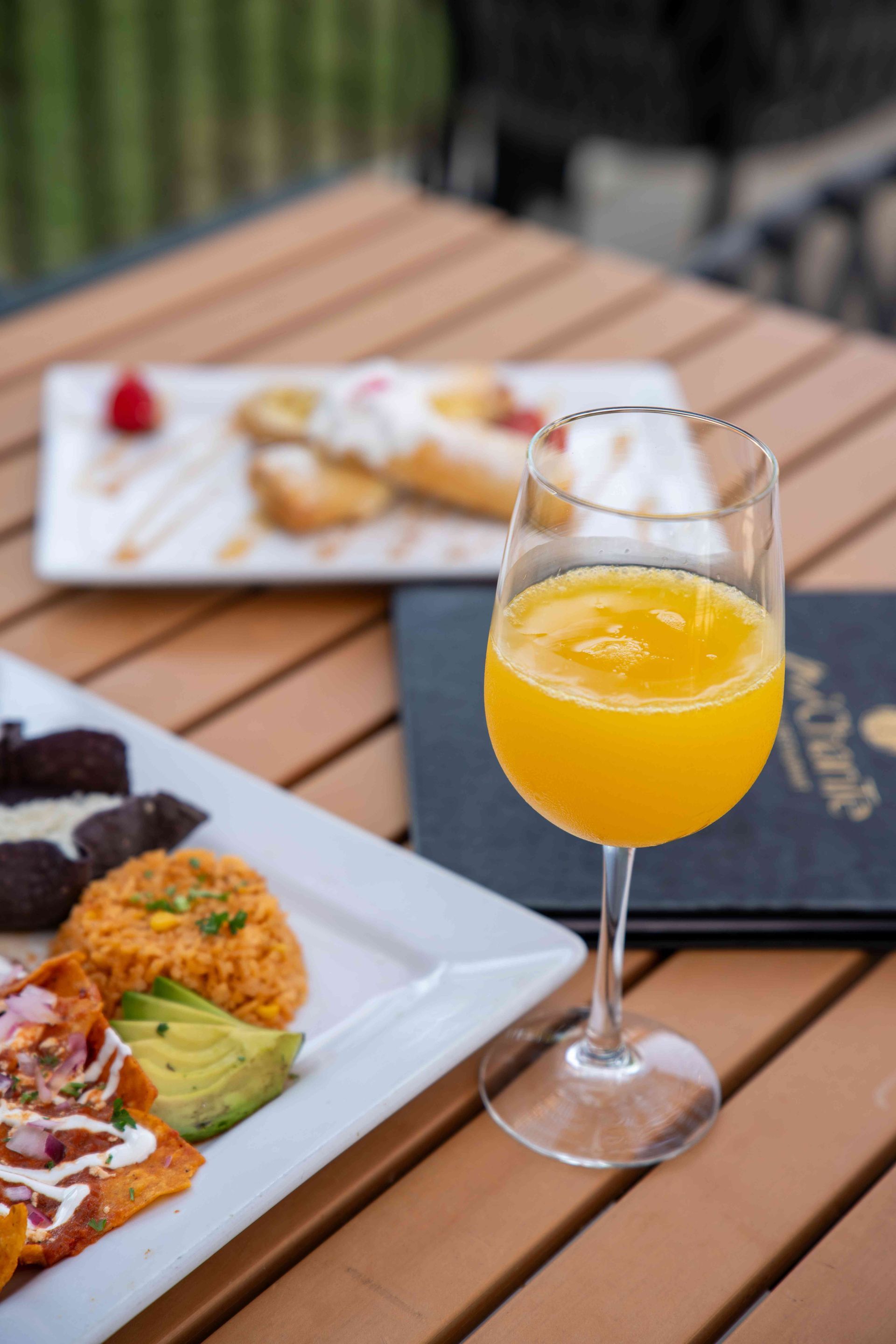 Brunch table: orange juice, plates of food, and menu on a wooden surface.