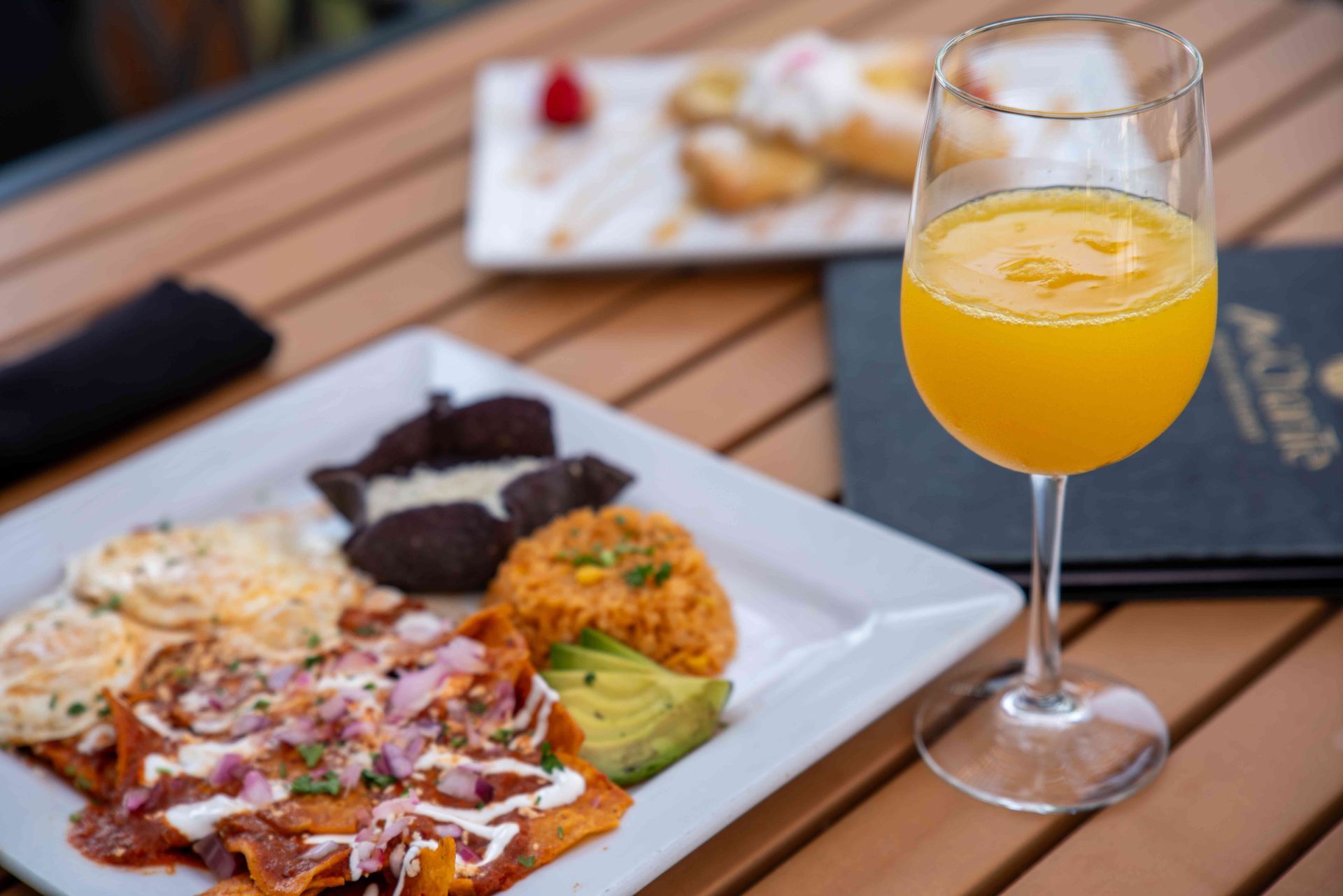 Brunch plate with eggs, chilaquiles, rice, avocado, and a mimosa on a wooden table.
