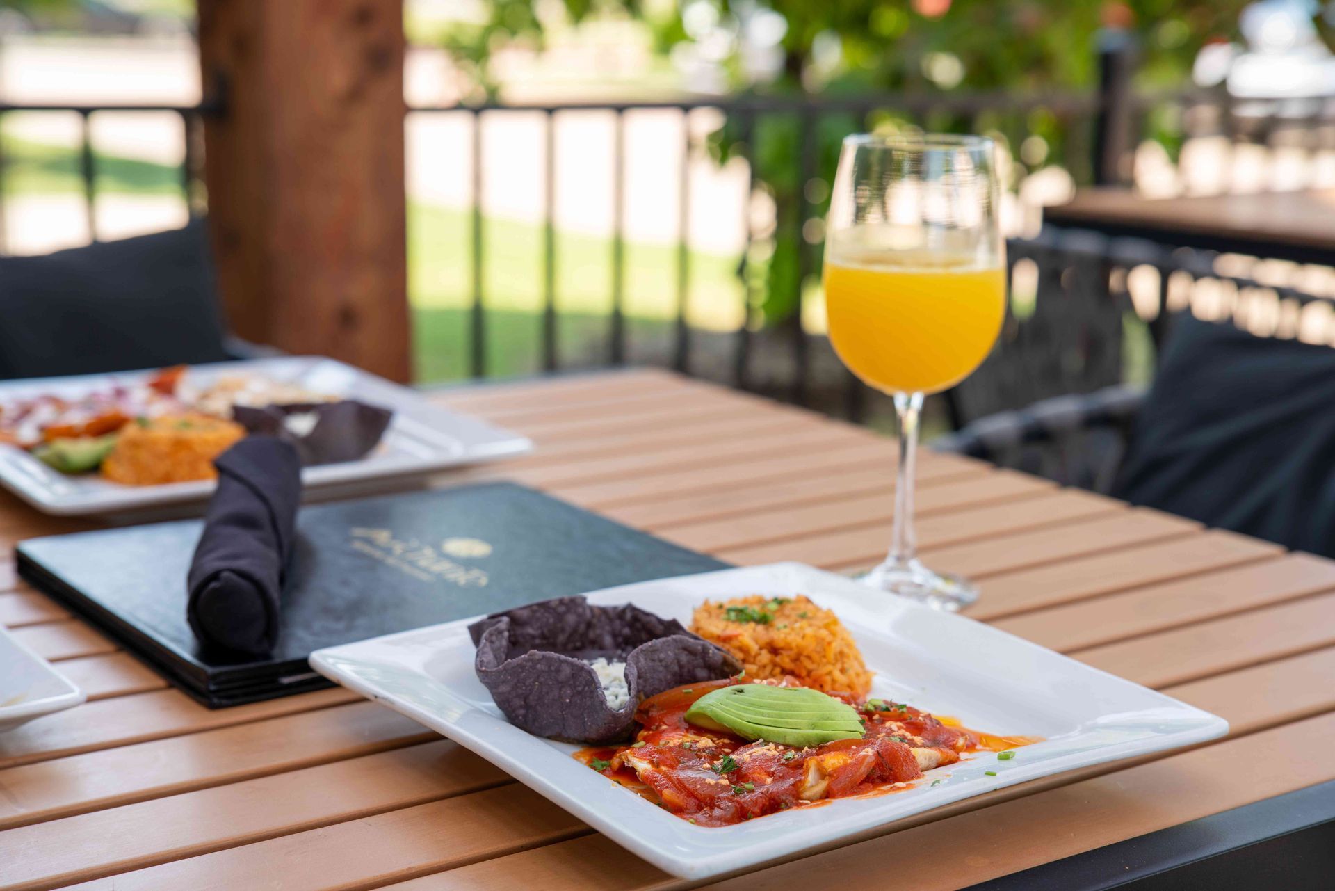 Outdoor table set with Mexican food, a mimosa, and menus.
