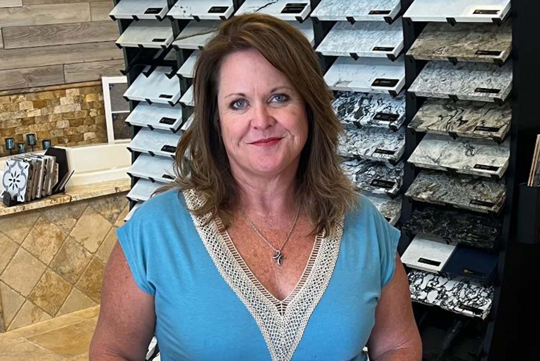 A woman in a blue shirt is standing in front of a display of granite tiles.