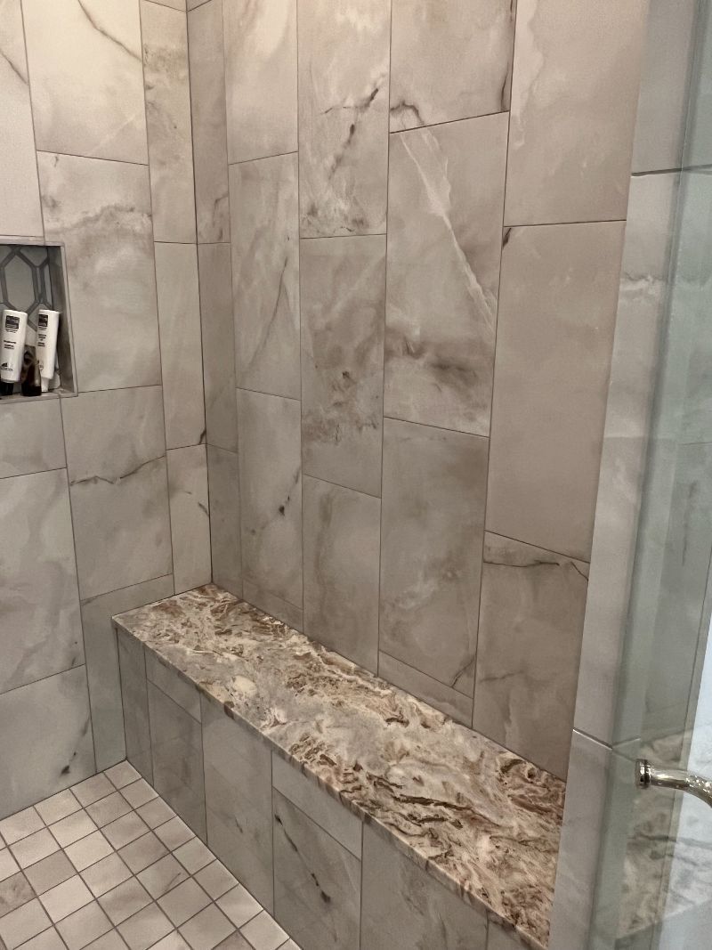 A bathroom with marble tiles and a bench in the shower.