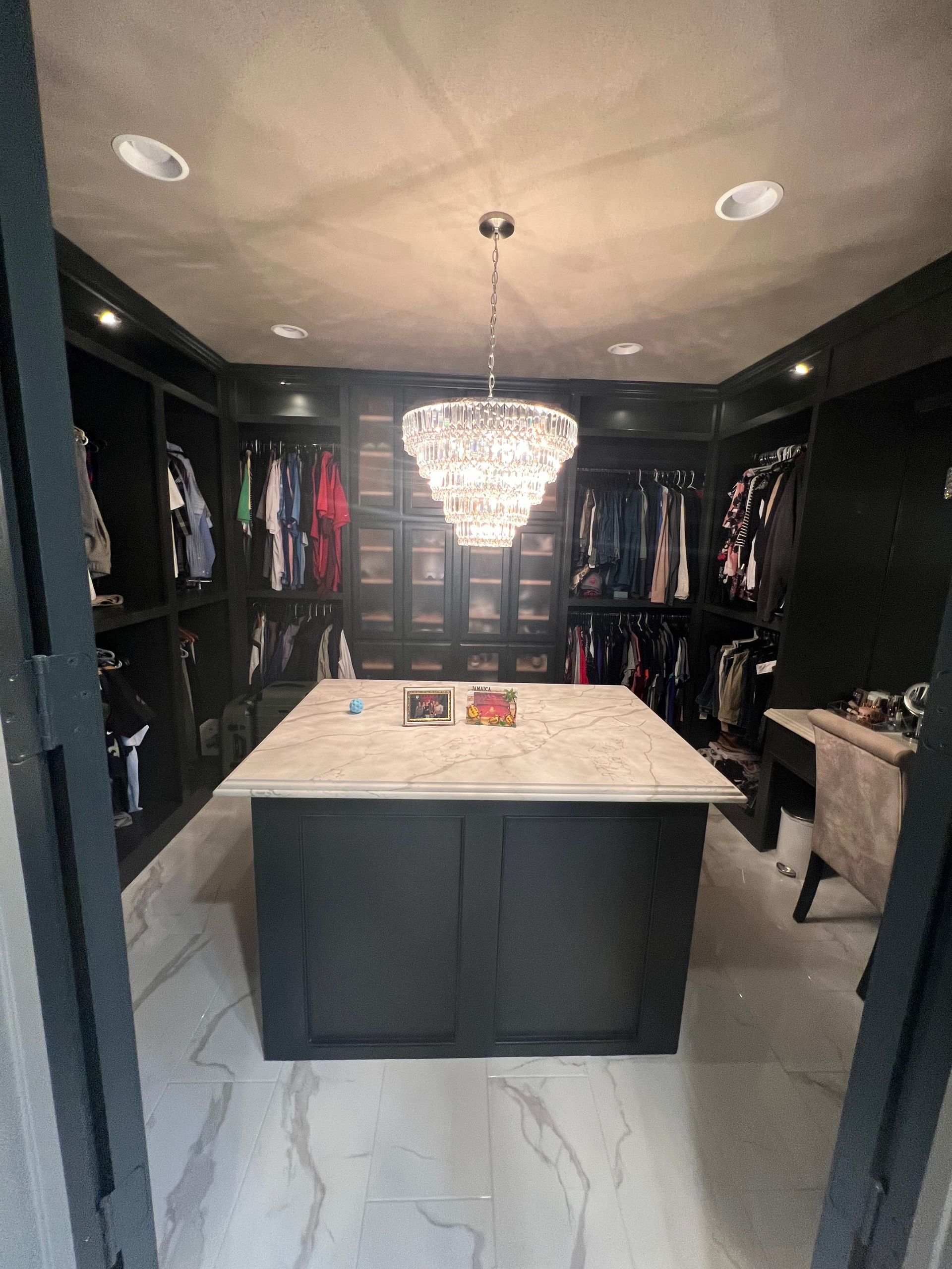 A walk in closet with a large island in the middle and a chandelier hanging from the ceiling.