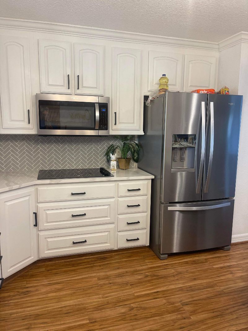 A kitchen with white cabinets , a stainless steel refrigerator , a microwave , and a stove.