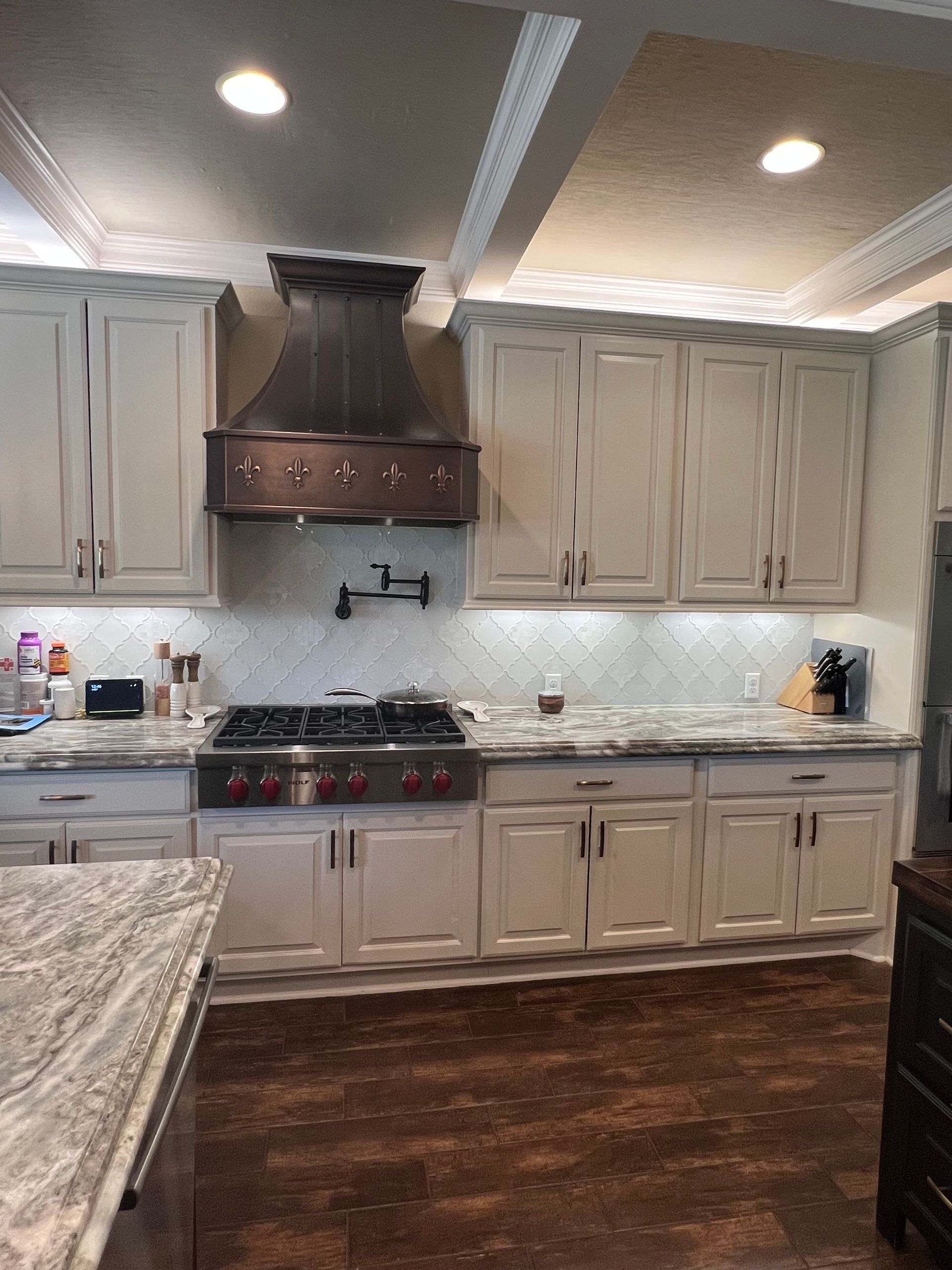 A kitchen with white cabinets , granite counter tops , a stove top oven , and a copper hood.