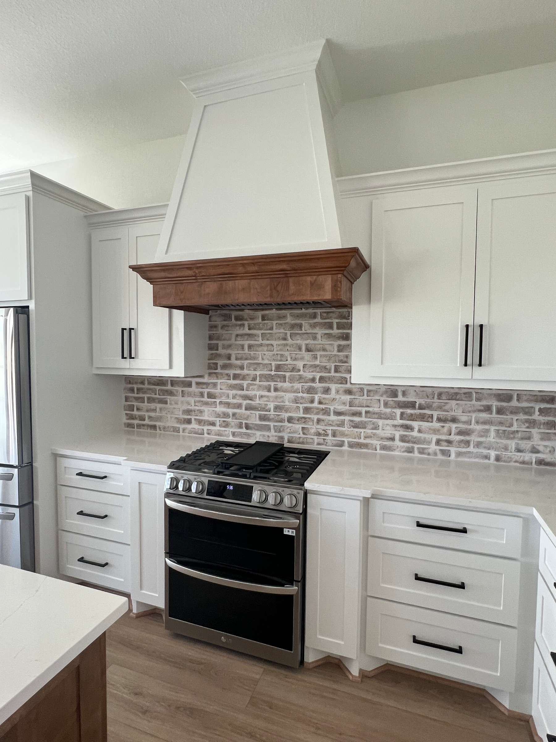 A kitchen with white cabinets , a stove , and a brick wall.