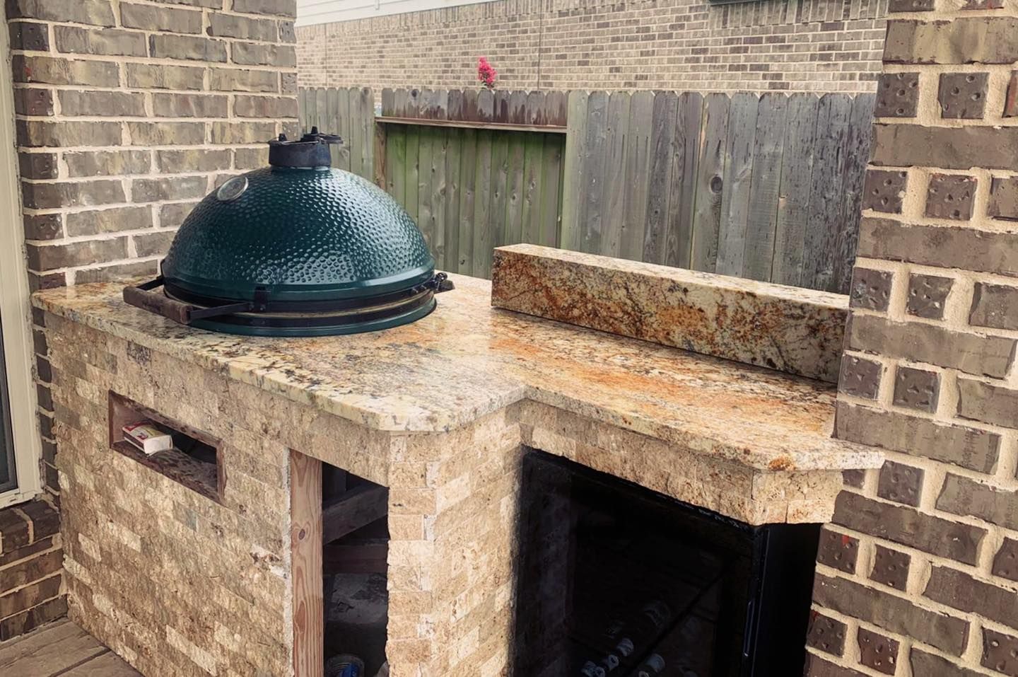A green egg grill is sitting on top of a granite counter next to a brick wall.