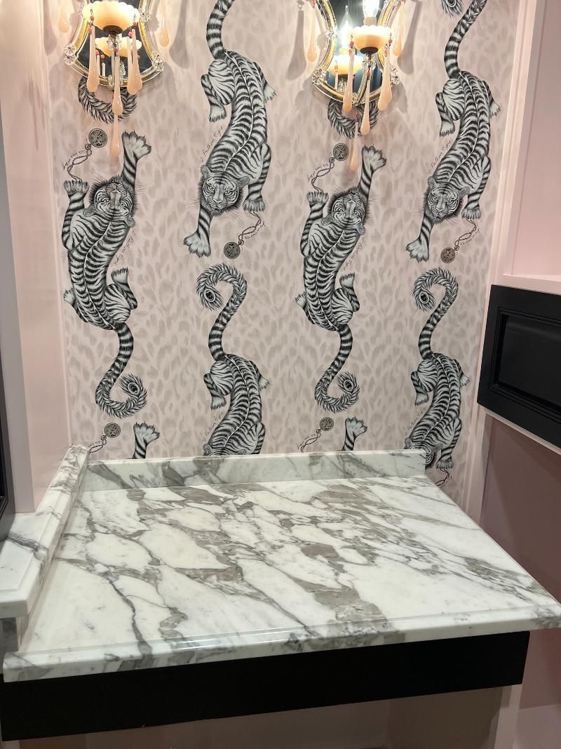 A bathroom with a marble counter top and tiger wallpaper on the wall.