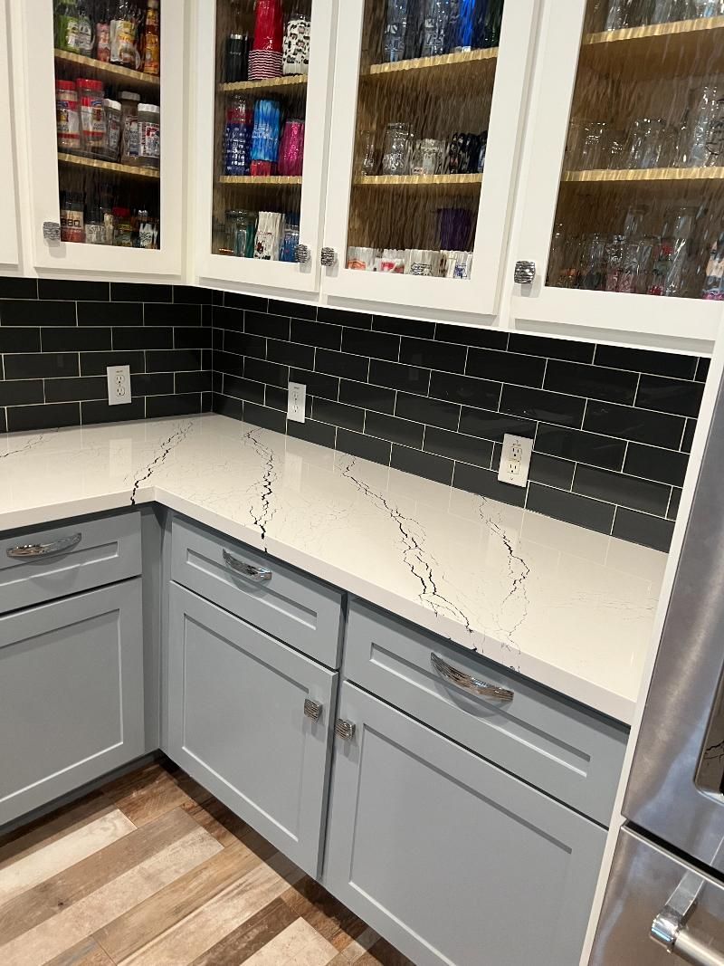 A kitchen with gray cabinets and white counter tops.