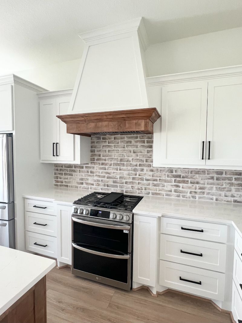 A kitchen with white cabinets , a stove , and a brick wall.