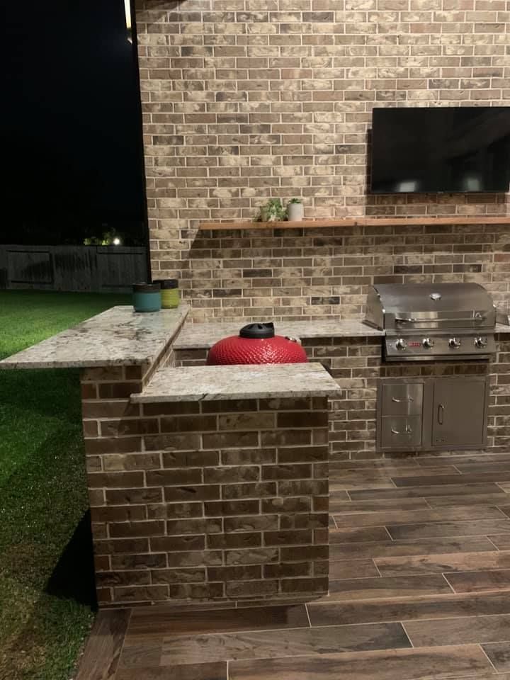 A brick outdoor kitchen with a grill and a television.