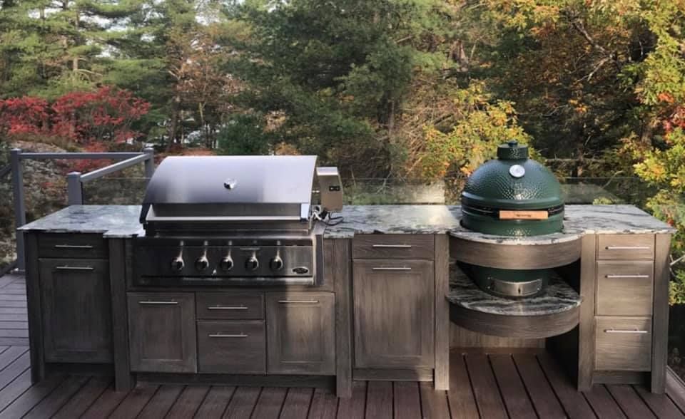 A large green egg grill is sitting on top of a wooden deck.