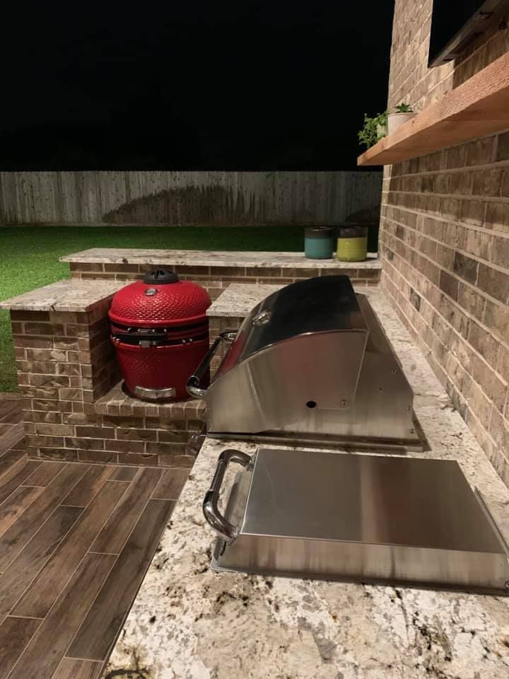 A stainless steel grill is sitting on top of a granite counter next to a brick wall.