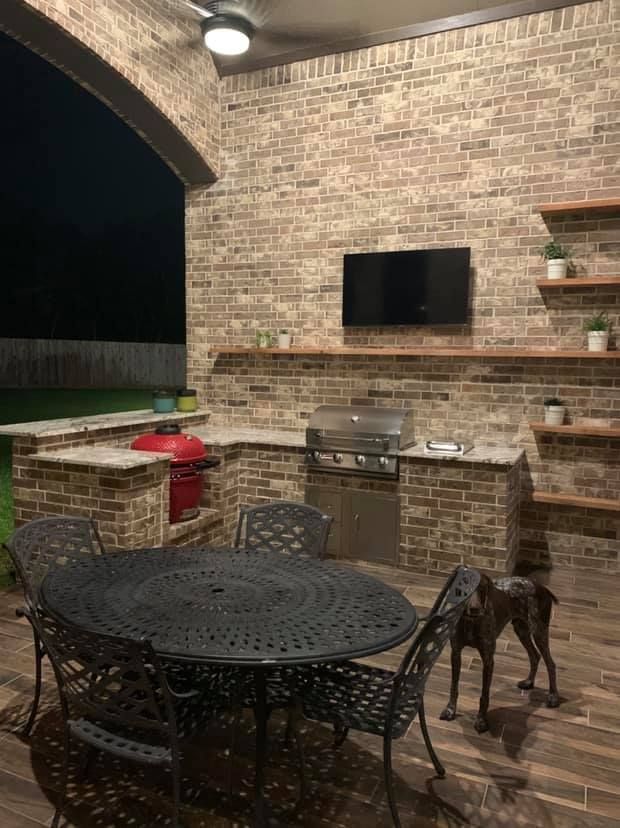 A dog is standing next to a table and chairs in an outdoor kitchen.