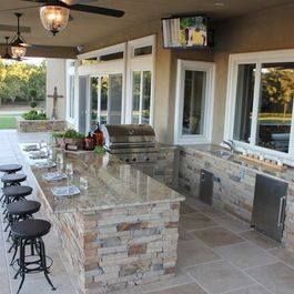 A kitchen with a large island , stools , a grill and a television on the ceiling.