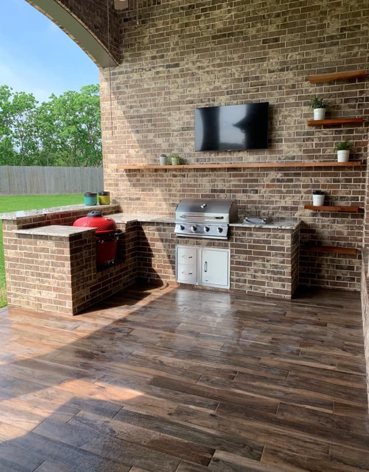 A brick outdoor kitchen with a grill and a flat screen tv.