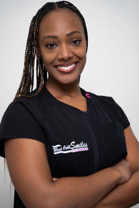 A woman wearing a black shirt with the word smiles on it is smiling with her arms crossed.