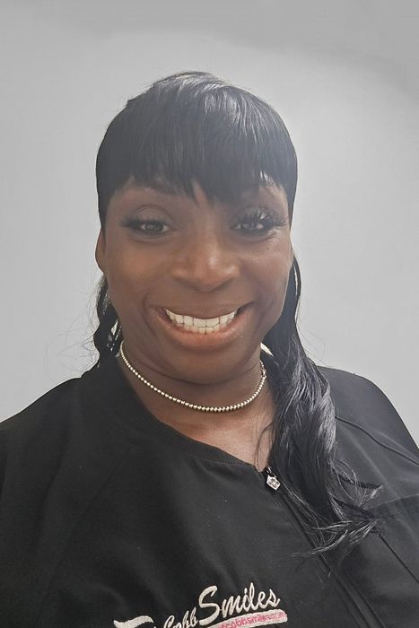 A woman wearing a black shirt and a necklace is smiling for the camera.