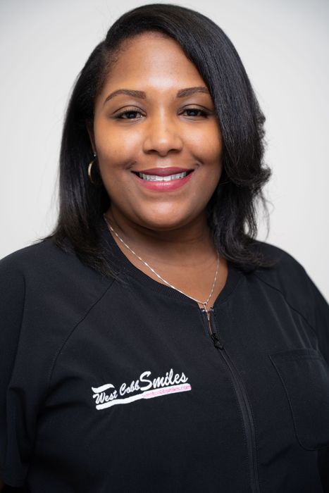 A woman wearing a black jacket with the word smiles on it is smiling for the camera.