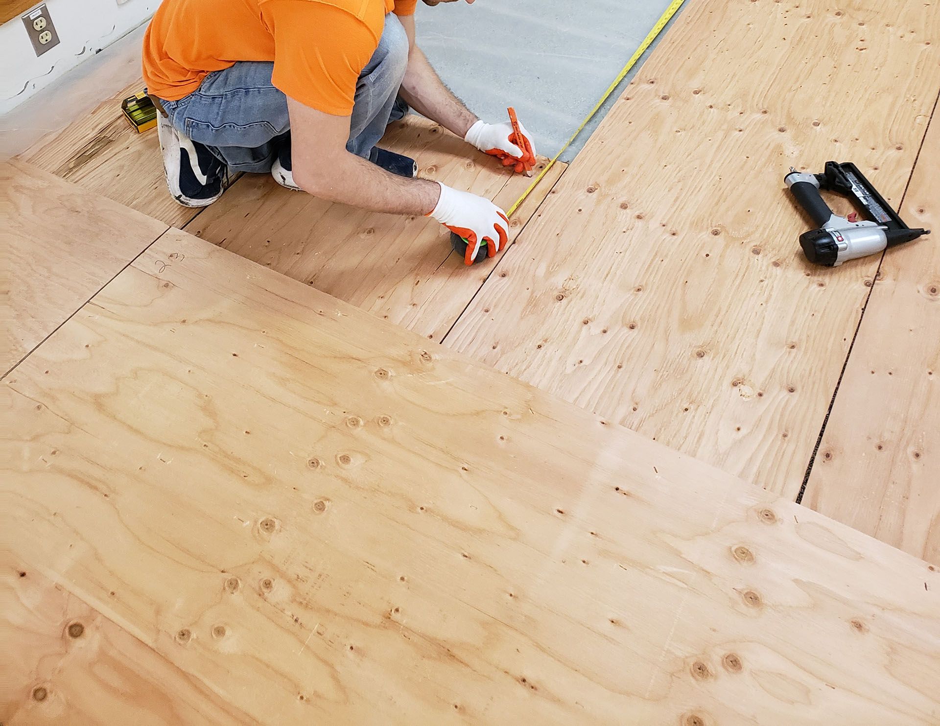 A man is measuring a piece of plywood with a tape measure
